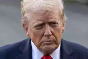 Hombre de cabello rubio y expresión seria usando traje oscuro y corbata roja