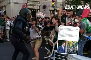 Un policía antidisturbios enfrenta a manifestantes en una protesta, mientras varias personas sostienen pancartas y una mujer intenta detener al agente, en la esquina superior derecha aparece el logo de un medio de noticias y una captura de pantalla de una publicación en redes sociales.