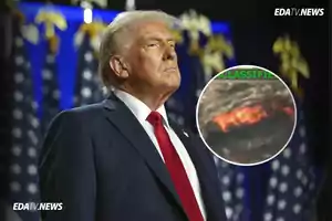 Hombre de cabello rubio con traje oscuro y corbata roja en primer plano con banderas de fondo y un recuadro circular mostrando una imagen borrosa con colores rojizos