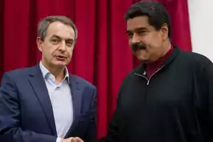 Dos hombres se dan la mano frente a una cortina roja