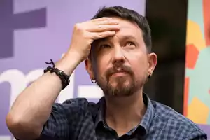 Un hombre con barba y camisa a cuadros se toca la frente mientras mira hacia arriba.