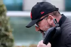 Hombre con gorra negra y barba sosteniendo una bolsa mientras camina al aire libre.