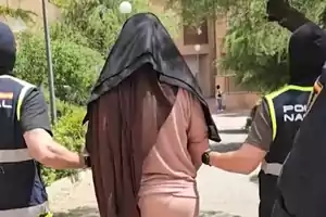 Una persona escoltada por dos agentes de policía con chalecos y pasamontañas en un entorno al aire libre